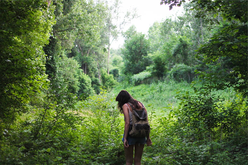 Young woman with backpack hiking through lush green forest