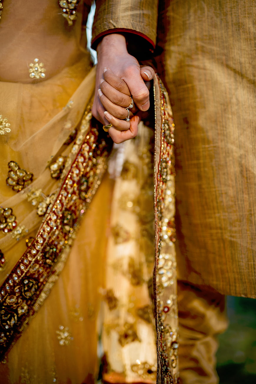 Close-up of couple holding hands in traditional gold wedding attire