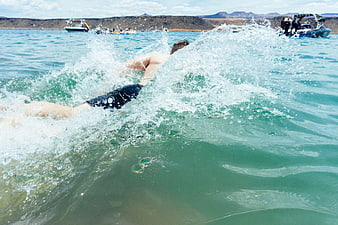 Man swimming in turquoise lake with boats and mountains