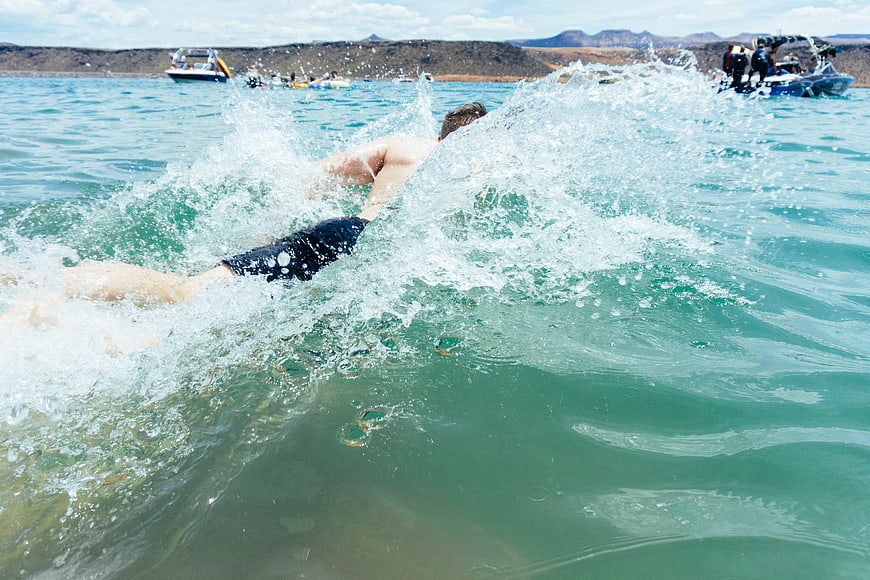 Man swimming in turquoise lake with boats and mountains
