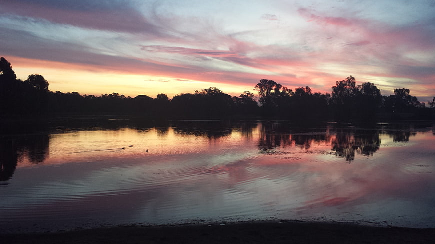 Serene Sunset Reflection on Calm Lake with Silhouetted Trees
