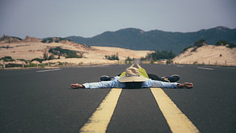 Man lying on desert road with mountains in background