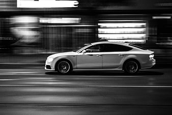 Black and white panning shot of a white sedan driving fast on a city street at night