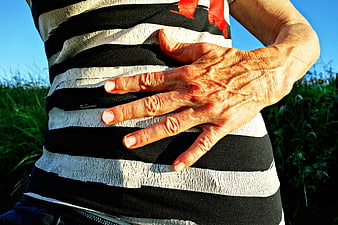 Close-up of senior woman's hand on striped top outdoors