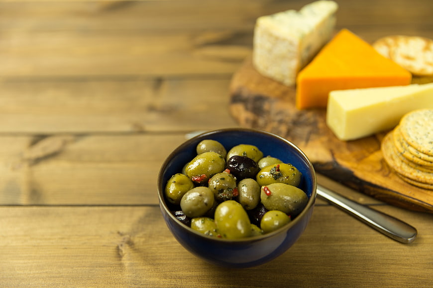 Bowl of marinated olives with cheese platter on wooden table