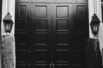 Symmetrical black and white photo of a grand wooden door with lanterns