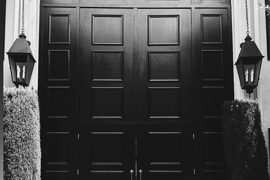 Symmetrical black and white photo of a grand wooden door with lanterns