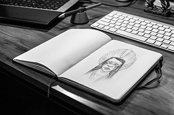 Pencil sketch of a face in an open notebook on a desk