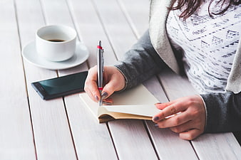 Woman writing in notebook with coffee and smartphone on wooden table