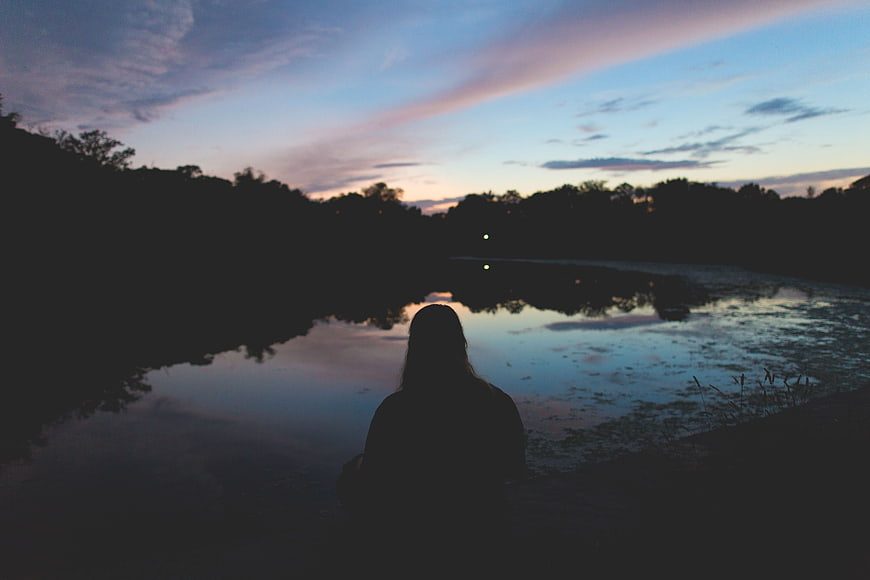 Silhouette of Woman Sitting by Lake at Dusk
