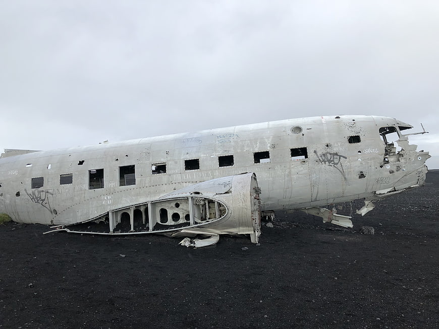 Crashed airplane fuselage on black sand beach with graffiti