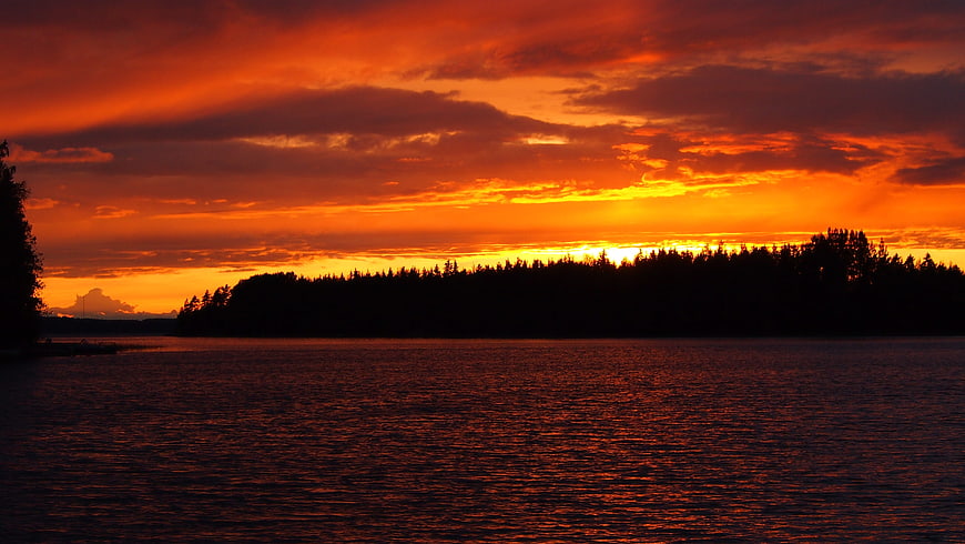 Vibrant Orange Sunset Over Silhouetted Lake and Forest