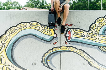 Skateboarder sitting on concrete wall with octopus graffiti