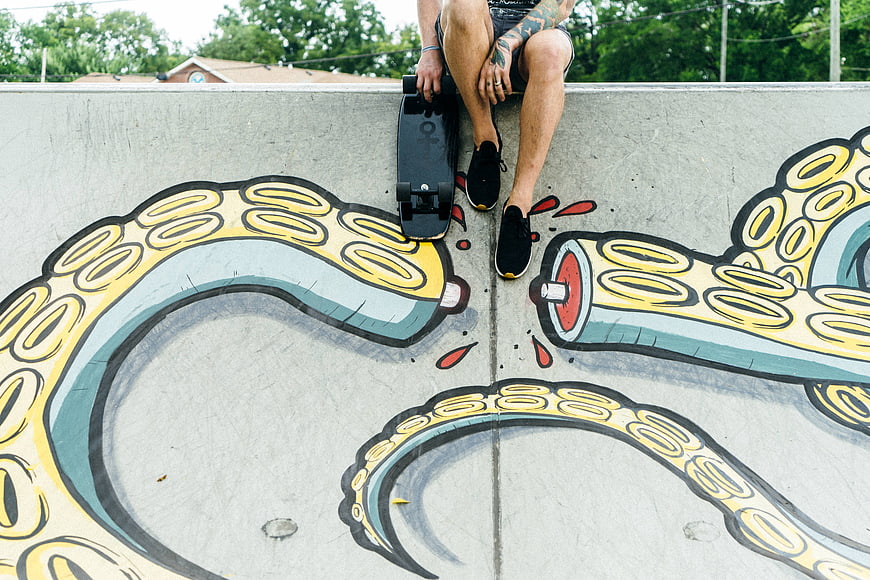Skateboarder sitting on concrete wall with octopus graffiti