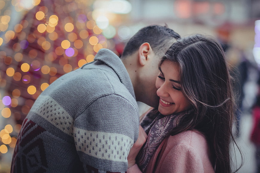 Happy couple kissing with Christmas bokeh lights background