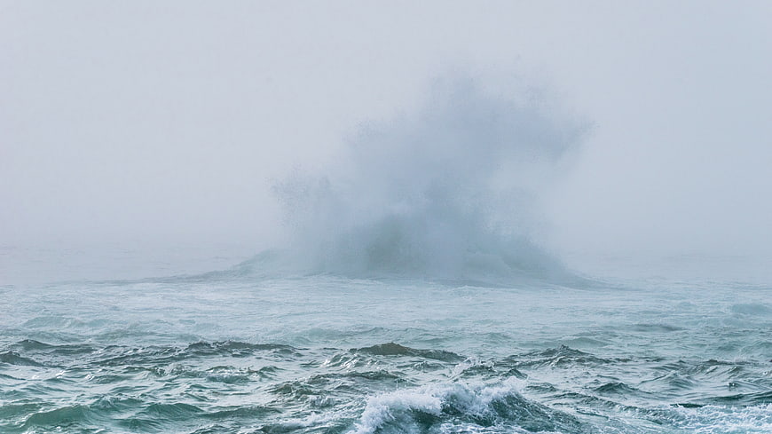 Majestic ocean wave crashing through thick fog and mist