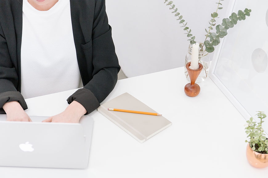 Woman typing on laptop at white minimalist office desk