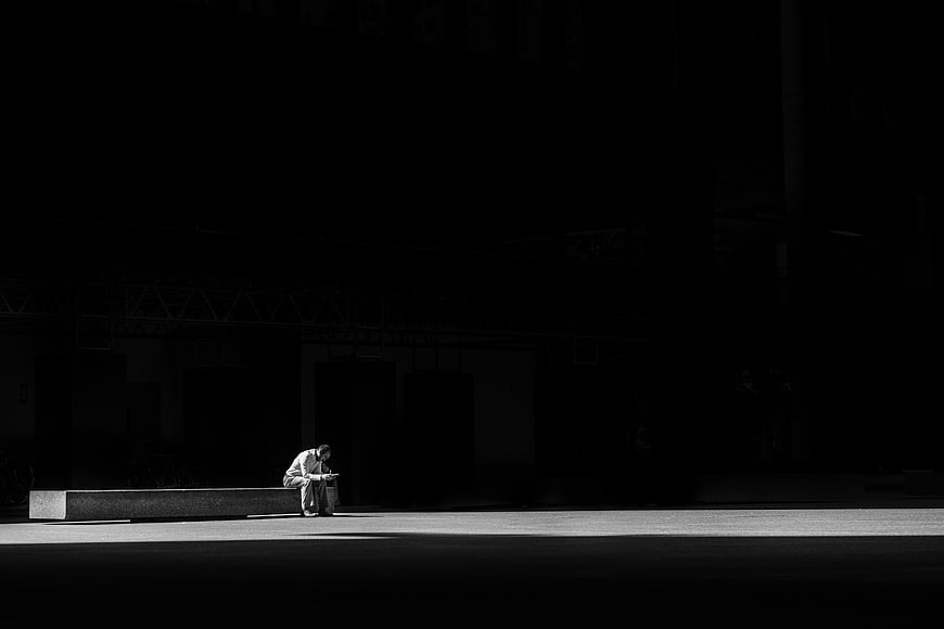 Lone man sitting on bench in dark urban plaza