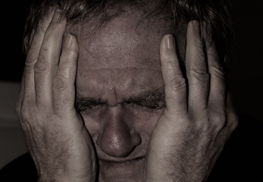 Close-up portrait of a distressed senior man holding his head in despair