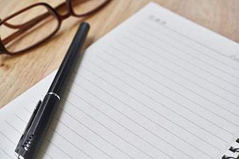 Black pen and glasses on a lined notebook page on a wooden desk