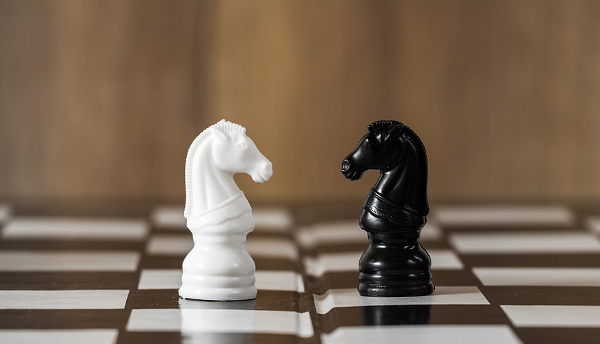 Black and white chess knights facing off on a wooden board
