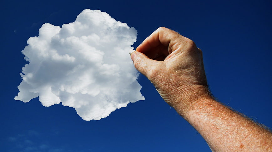 Hand holding a cloud against a blue sky background