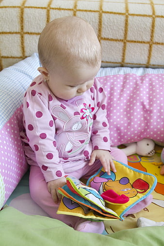 Baby girl reading colorful cloth book on bed