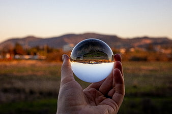 Hand holding crystal ball reflecting landscape at sunset