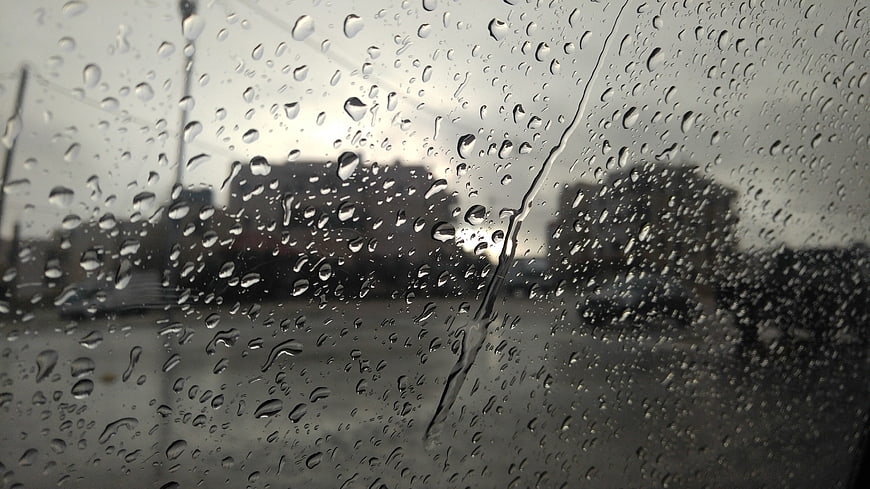 Raindrops on car windshield with blurred city background