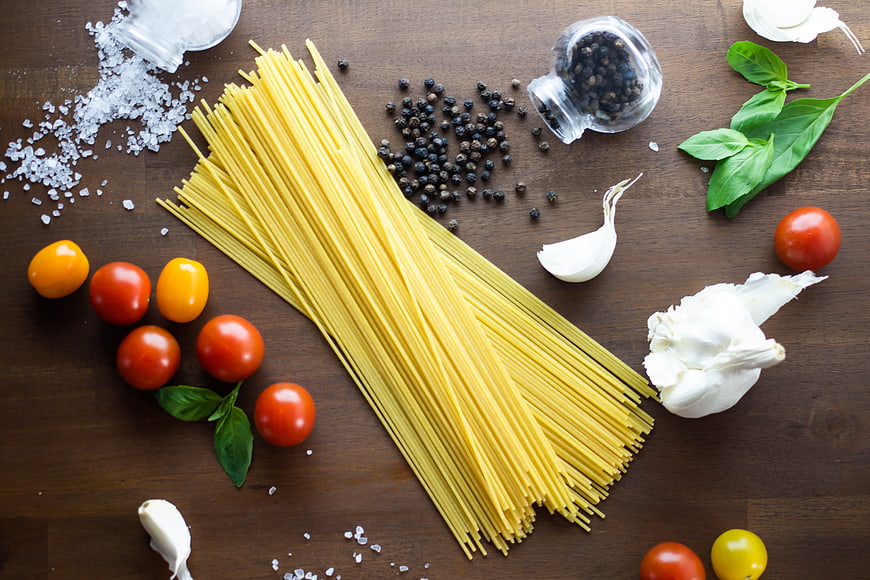 Uncooked spaghetti with fresh tomatoes, basil, garlic, and spices on wood