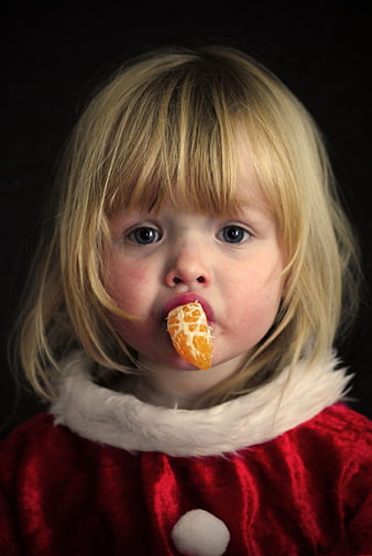 Cute toddler girl in Santa suit eating mandarin orange