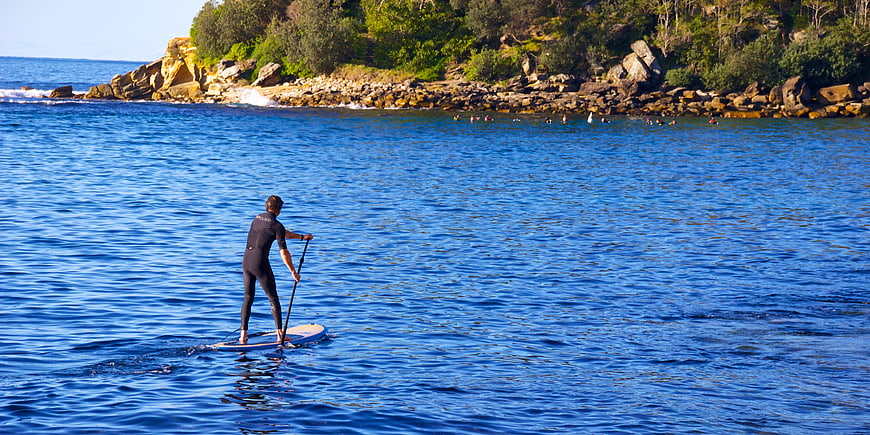 Man Paddleboarding on Blue Ocean Near Rocky Coastline