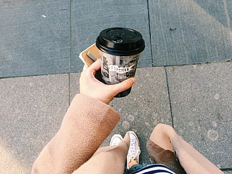 First-person view of woman holding coffee cup on street