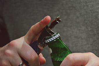 Close-up of hands opening a green beer bottle with a corkscrew