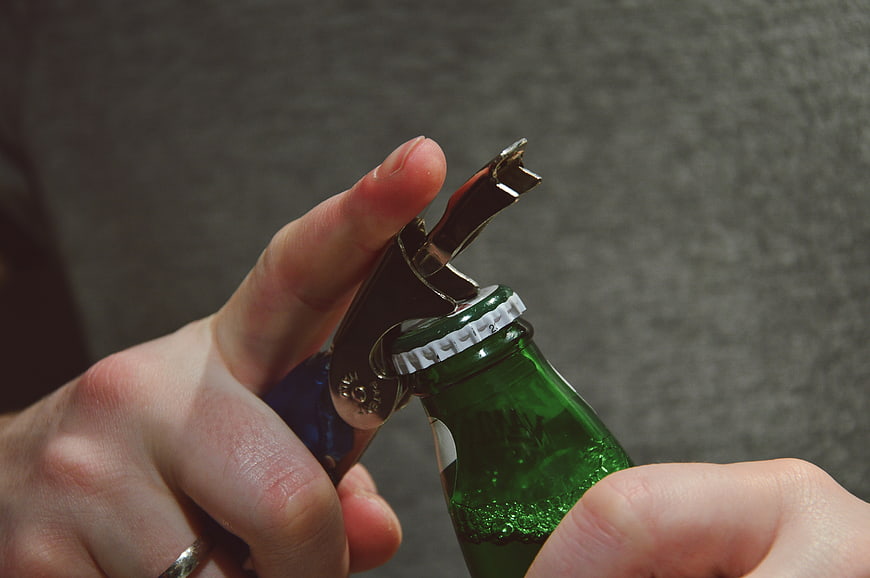 Close-up of hands opening a green beer bottle with a corkscrew