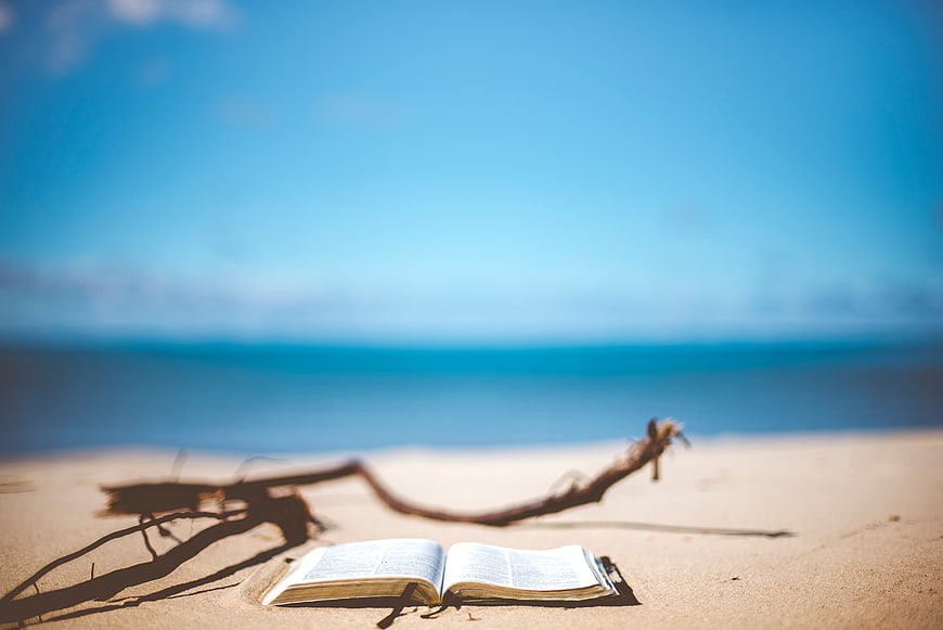 Open Bible on Sandy Beach with Ocean Background