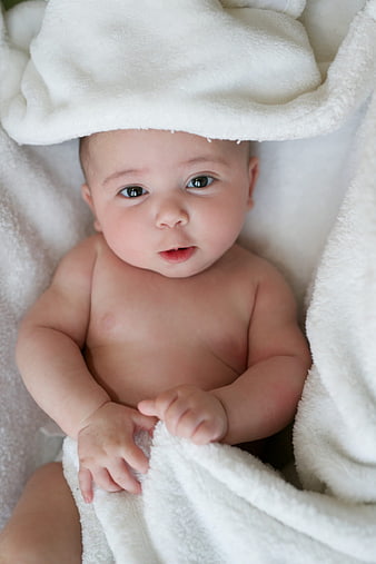 Adorable newborn baby wrapped in white towel looking up