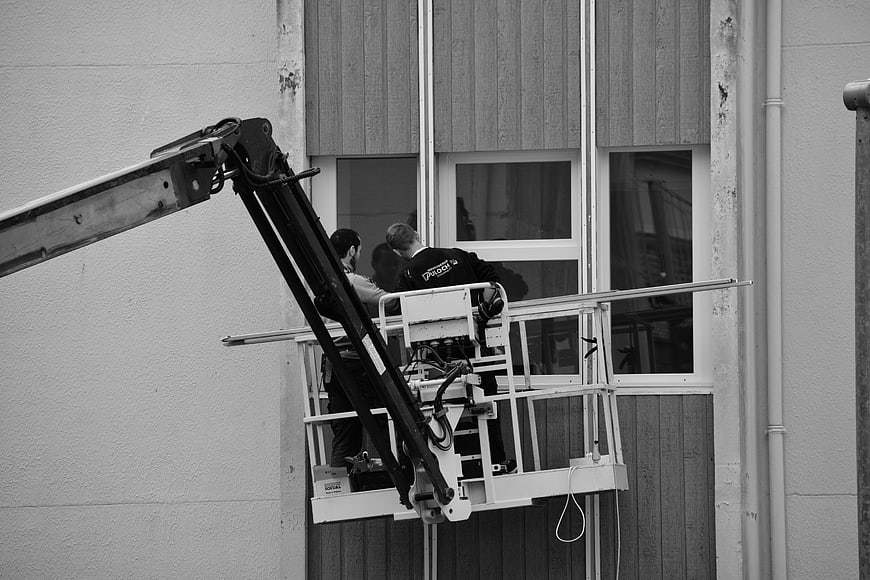 Workers installing windows on a building facade using a lift