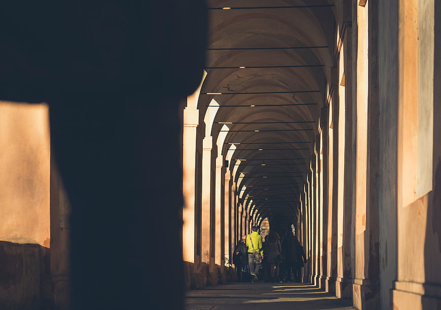 People Walking Through Sunlit Arched Colonnade