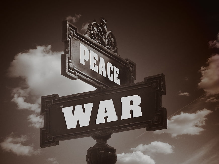 Vintage street sign pointing to peace and war against cloudy sky