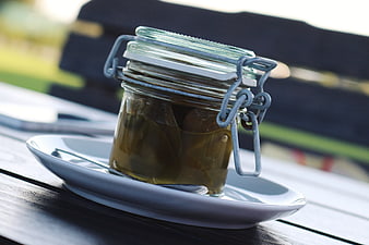 Glass jar of pickled jalapenos on white plate outdoors
