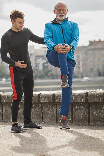 Senior man stretching leg with young trainer outdoors