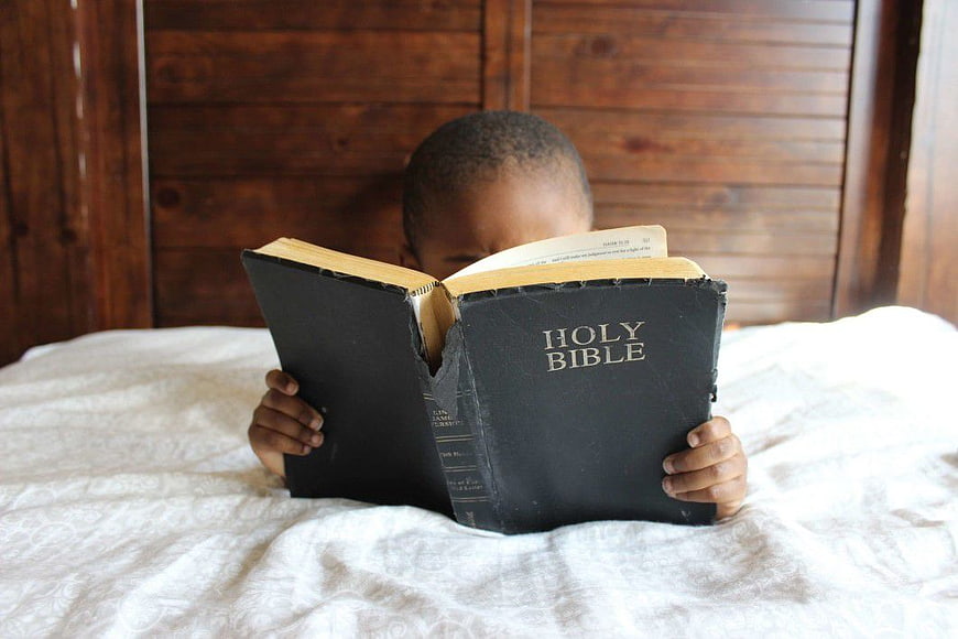 Young Boy Reading Holy Bible in Bed