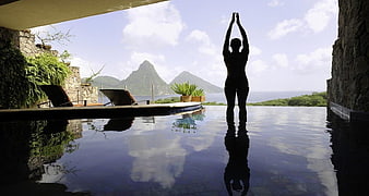 Woman practicing yoga at infinity pool with tropical mountain view