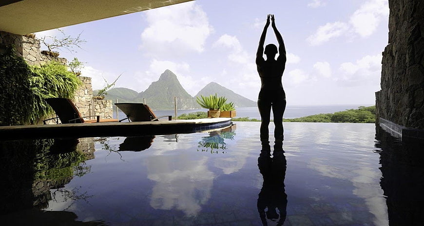 Woman practicing yoga at infinity pool with tropical mountain view
