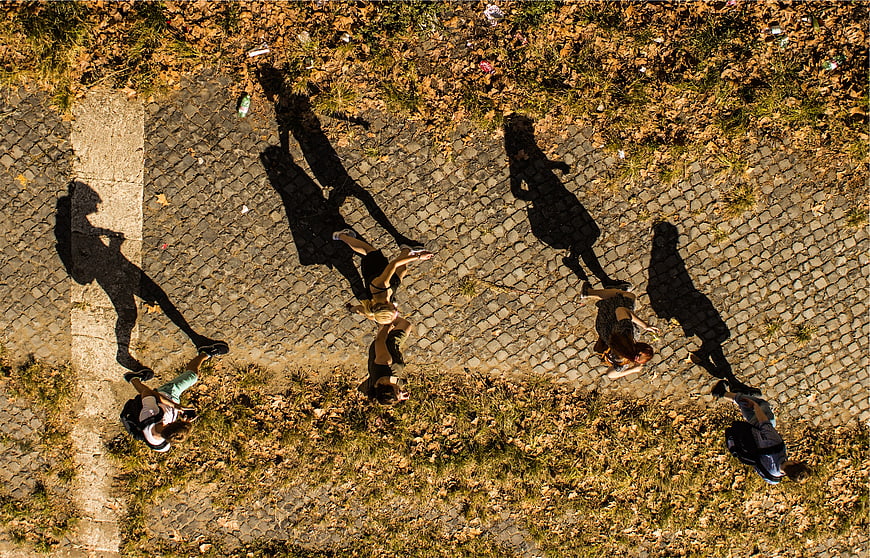 Aerial view of people walking on cobblestone path with long shadows