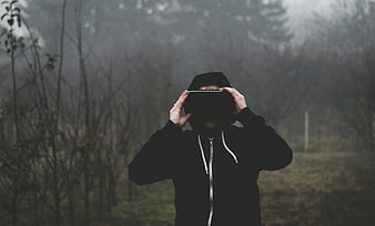 Man in black hoodie holding VR headset in foggy forest