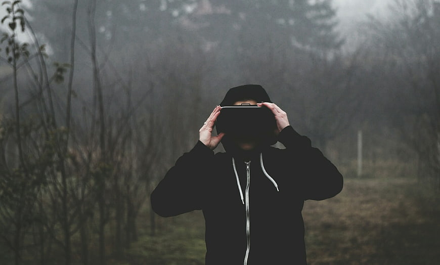 Man in black hoodie holding VR headset in foggy forest