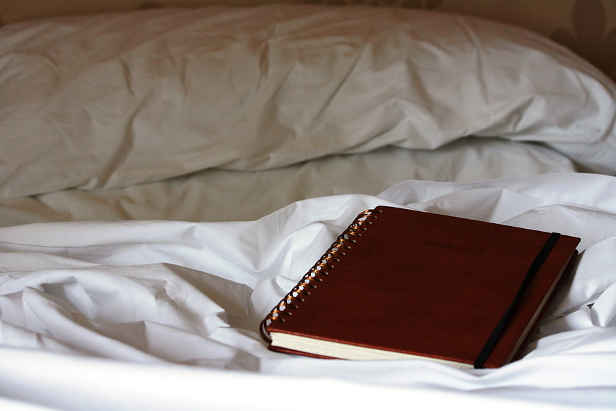 Brown spiral notebook resting on white bed sheets