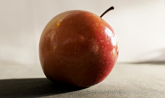 Close-up of a shiny red apple on a textured surface